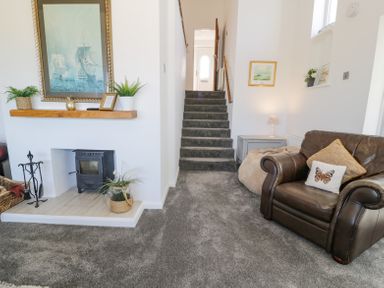 A living room with a staircase a leather armchair a fireplace with plants and a painting at Minerva in Trearddur Bay