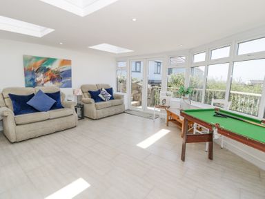 A sitting area with two beige armchairs with cushions a small snooker table and large windows at Minerva in Trearddur Bay