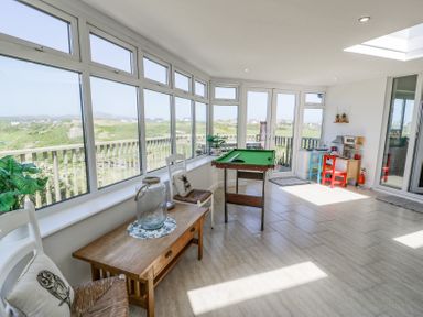 A sunroom with multiple windows a small pool table a wooden table two chairs and a children's play area at Minerva in Trearddur Bay