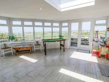 A sunroom with large windows a small pool table two chairs a coffee table and a small play area with a desk at Minerva in Trearddur Bay