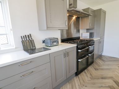 A kitchen with grey cabinets a gas stove a toaster a microwave and a knife set at Minerva in Trearddur Bay