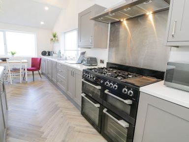 A kitchen with gray cabinets a black stove a microwave and a dining table with white chairs and a red chair at Minerva in Trearddur Bay