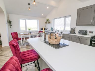 A kitchen with an island countertop and red chairs a dining table with white chairs and red chairs and gray cabinets at Minerva in Trearddur Bay