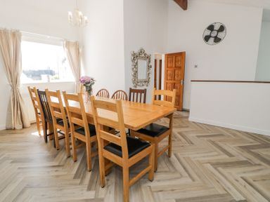 A dining room with a long wooden table and chairs by a window with curtains and a wall mirror at Minerva in Trearddur Bay