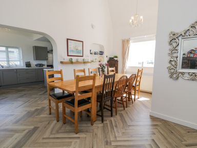 A dining area with a wooden table and mixed chairs near a window and an open doorway to a kitchen at Minerva in Trearddur Bay