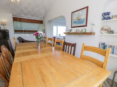 A dining room with a long wooden table and chairs a vase with flowers on the table bookshelves and wall decorations at Minerva in Trearddur Bay
