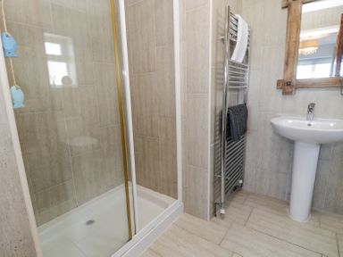 A bathroom with a shower cubicle a pedestal sink a towel radiator with towels and a wooden framed mirror at Minerva in Trearddur Bay
