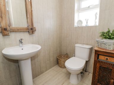 A bathroom with a sink a toilet a wicker basket a wooden cabinet and a window with decorations at Minerva in Trearddur Bay