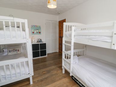 A bedroom with two white bunk beds a small cabinet and a wooden door at Minerva in Trearddur Bay