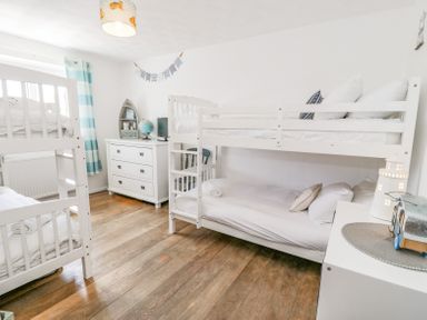 A bedroom with two white bunk beds a white chest of drawers and a wooden floor at Minerva in Trearddur Bay