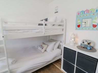 A small bedroom with a white bunk bed and a storage unit with decorative items at Minerva in Trearddur Bay