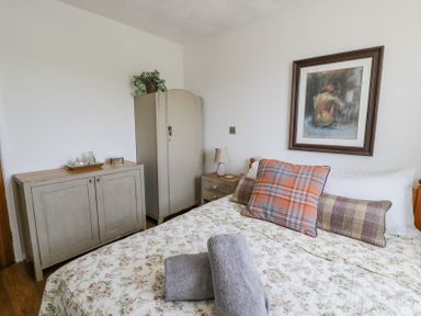 A bedroom with a bed pillows and towels a cabinet a wardrobe and a framed painting on the wall at Minerva in Trearddur Bay