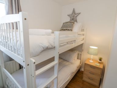 A bedroom with a white bunk bed two pillows a bedside table with a lamp and a small plant at Minerva in Trearddur Bay