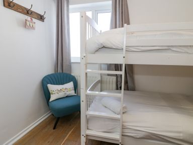 A small bedroom with a white bunk bed a blue chair with a cushion and a wooden floor at Minerva in Trearddur Bay