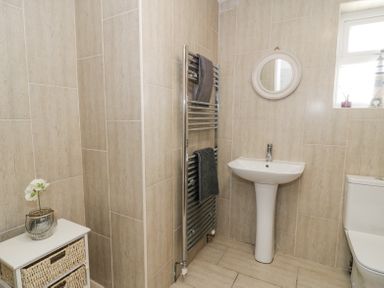A bathroom with a pedestal sink a toilet a towel rack with towels a small cabinet with drawers and a window at Minerva in Trearddur Bay