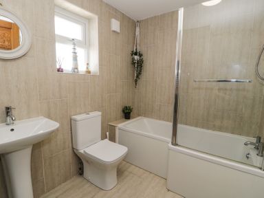 A bathroom with a pedestal sink toilet bathtub shower curtain and small plants at Minerva in Trearddur Bay