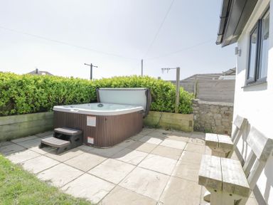 An outdoor patio area with a hot tub and steps next to a wooden bench at Minerva in Trearddur Bay