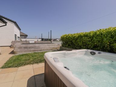 A hot tub next to a grassy area and wooden planters outside a white building at Minerva in Trearddur Bay