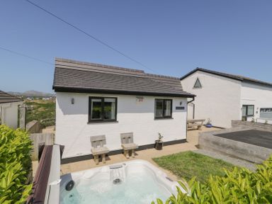 An outdoor area with a white building two wooden chairs a hot tub and a trampoline at Minerva in Trearddur Bay