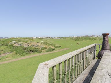 A wooden balcony railing overlooking a grassy field with cows and houses in the distance at Minerva in Trearddur Bay