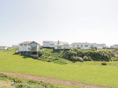 Row of houses on a grassy hillside with shrubs at Minerva in Trearddur Bay