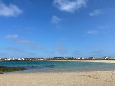 A sandy beach with calm water and houses in the distance at Minerva in Trearddur Bay