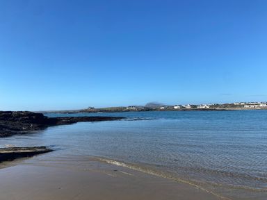 A beach with water and rocks with houses and hills in the background at Minerva in Trearddur Bay