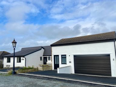 A white house with black doors and windows a garage door and a street lamp outside at Minerva in Trearddur Bay