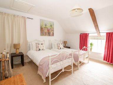 A bedroom with two single beds bedside tables lamps a wooden chair and curtains at Manor Farm Cottage in Swaffham