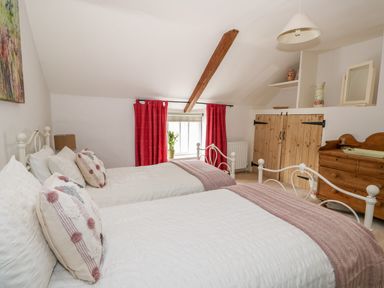 A bedroom with two single beds white bedding and red curtains at Manor Farm Cottage in Swaffham