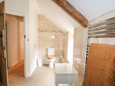 A bathroom with a toilet wooden toilet seat towel rack with brown towel and a small white table at Manor Farm Cottage in Swaffham