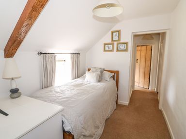 A bedroom with a bed a lamp a chest of drawers and framed pictures on the wall at Manor Farm Cottage in Swaffham