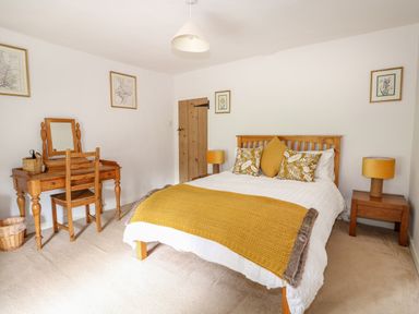 A bedroom with a wooden bed and yellow decor a wooden dressing table with mirror and chair at Manor Farm Cottage in Swaffham