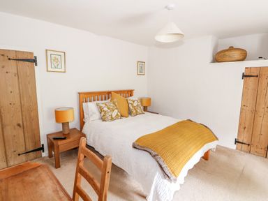 A bedroom with a wooden bed with white bedding and yellow pillows and blanket at Manor Farm Cottage in Swaffham