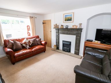 A living room with two leather sofas a decorative fireplace a television on a wooden stand and a window at Manor Farm Cottage in Swaffham