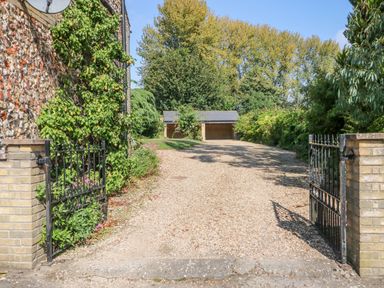A gravel driveway with black metal gates open and trees in the background at Manor Farm Cottage in Swaffham
