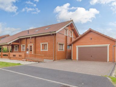A wooden house with a tiled roof and attached garage with driveway at Jamaal Lodge in South Broomhill near Amble