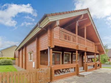 A wooden house with a covered porch and balcony in a residential area at Jamaal Lodge in South Broomhill near Amble