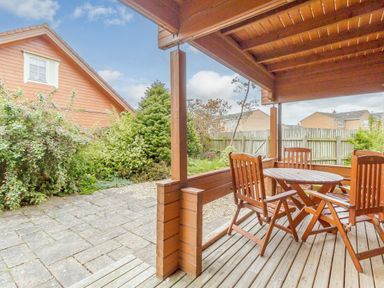 A covered wooden patio with a round table and four chairs overlooking a garden with bushes and wooden fences at Jamaal Lodge South Broomhill near Amble