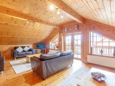 A living room with leather sofas coffee table television and large windows at Jamaal Lodge in South Broomhill near Amble