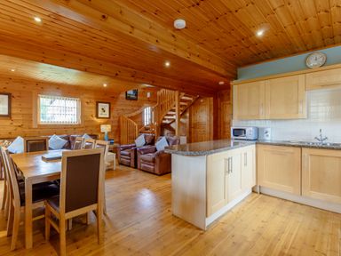 An open plan wooden interior with a kitchen island dining table chairs leather armchairs and a staircase at Jamaal Lodge South Broomhill near Amble