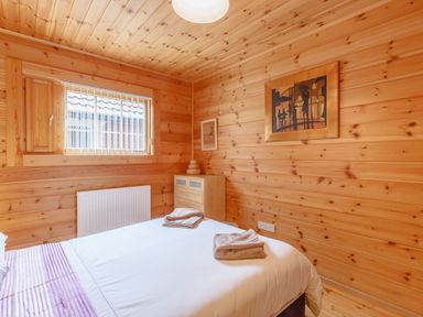 A bedroom with a bed and neatly folded towels a wooden chest of drawers and a window with blinds at Jamaal Lodge in South Broomhill near Amble