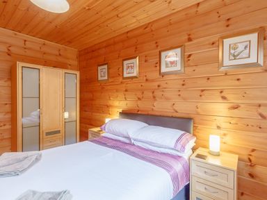 A bedroom with a bed a wooden wardrobe bedside tables and framed pictures on wooden walls at Jamaal Lodge South Broomhill near Amble