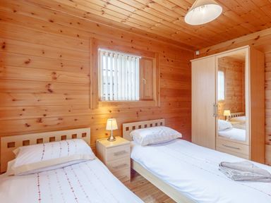 A bedroom with two single beds a bedside table with a lamp a wardrobe with a mirror and wooden walls at Jamaal Lodge in South Broomhill near Amble