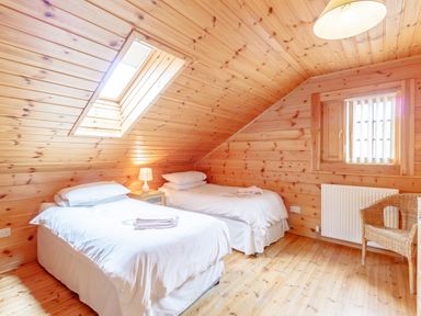 A bedroom with two single beds with white bedding a skylight window a table lamp a wicker chair and wooden walls and ceiling at Jamaal Lodge South Broomhill near Amble