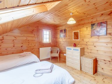 A bedroom with two beds a wooden dresser a chair and a laundry basket at Jamaal Lodge in South Broomhill near Amble