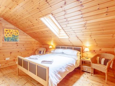 A bedroom with a double bed two wicker chairs wooden walls ceiling and floor and skylight at Jamaal Lodge in South Broomhill near Amble