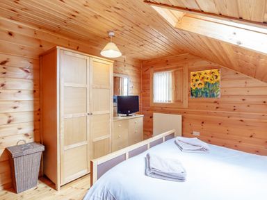 A bedroom with wooden walls and ceiling a bed with folded towels a wardrobe a chest of drawers a small television a window and a painting at Jamaal Lodge South Broomhill near Amble