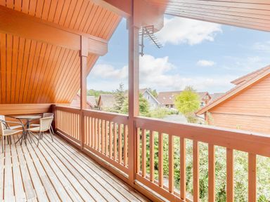 A wooden balcony with two wicker chairs and a round glass table overlooking houses and greenery at Jamaal Lodge in South Broomhill near Amble