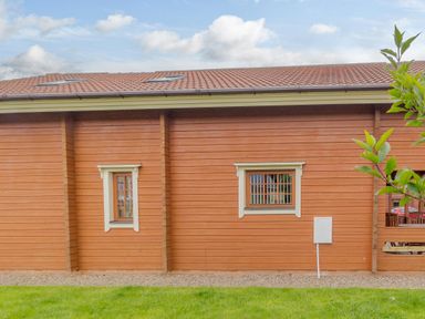 An exterior view of a wooden building with two windows and a grassy area in front at Jamaal Lodge in South Broomhill near Amble